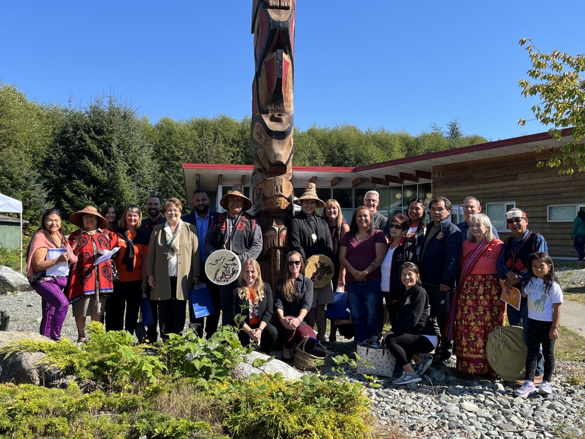 Picture of a group of people standing by a totem pole in Pacheedaht Nation.